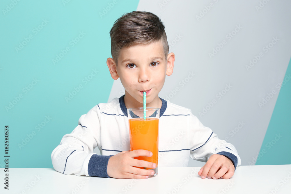 Cute little boy drinking juice while sitting at table, on color background Cute little boy drinking juice while sitting at table, on color background
