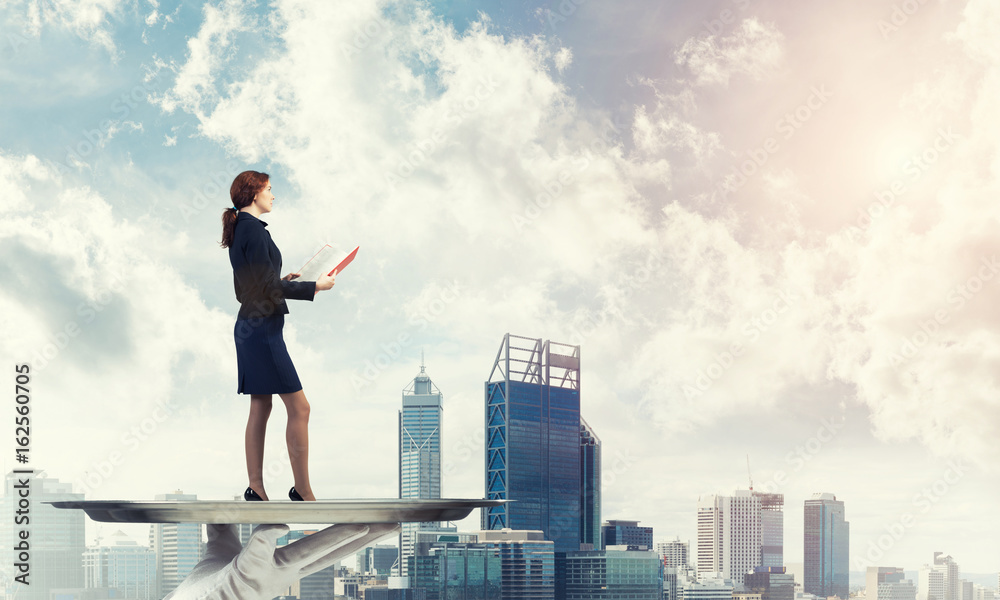 Attractive businesswoman on metal tray with red book in hands against cityscape background Attractive businesswoman on metal tray with red book in hands against cityscape background
