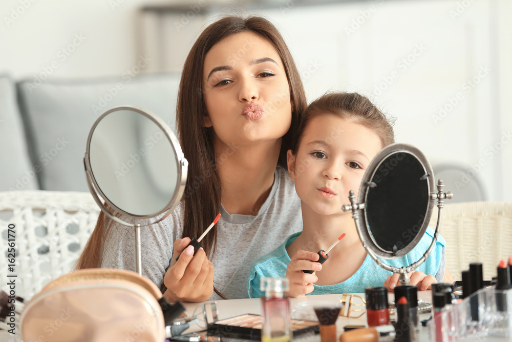 Young woman and her little daughter applying makeup at home