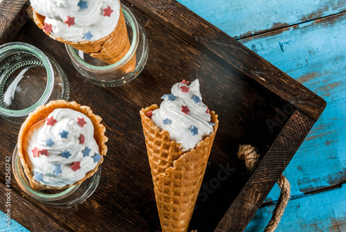 Treats for Independence Day holiday on July 4. Homemade cream ice cream in waffles, decorated with stars in traditional colors - blue, red, white. On a blue old wooden table, copy space top view