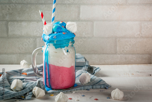 Treats for Independence Day holiday, July 4. Homemade milkshake, crazy shake with ice cream, in traditional colors - blue, red, white, decorated with stars. meringues. On white home table, copy space photo