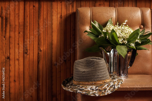 men's straw hat and an old kettle with a bouquet of lilies of the valley on a brown wooden background photo