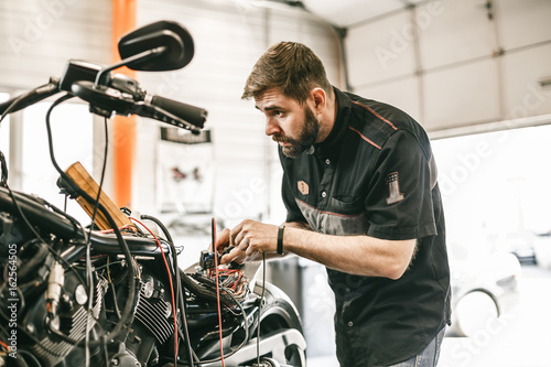 Motorcycle mechanic repairing electronics sports black bike. Handsome mechanic working in auto repair shop.