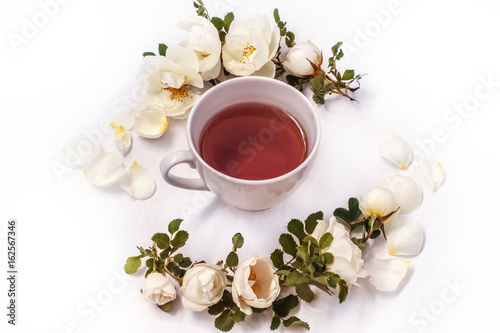 Cup of black tea with white flowers rose hips on a white background