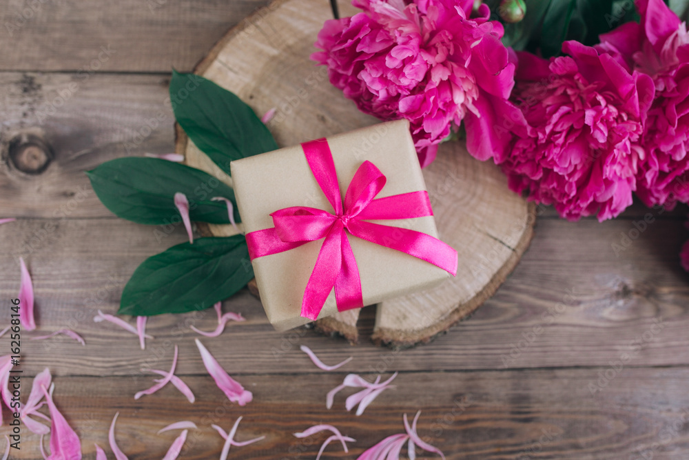 Row of peonies and gift box on wooden background with space for message. Women's or Mother's Day background. Top view Row of peonies and gift box on wooden background with space for message. Women's or Mother's Day background. Top view