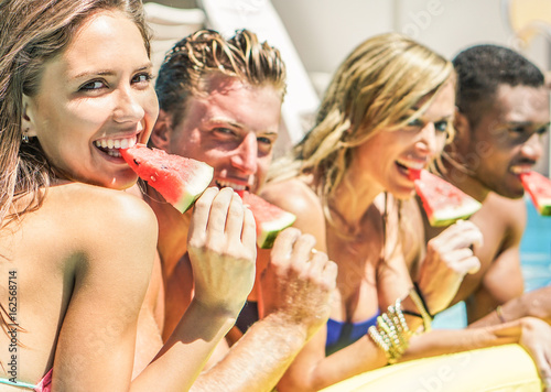 Happy friends eating watermelon in swimming pool hotel resort -  Diverse culture couples having fun in summer vacation - Travel, youth, holidays concept - Focus on left girl - Warm contrast filter