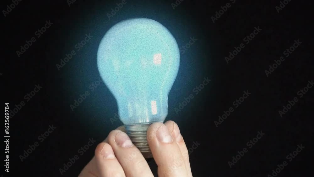 the bulb lights up in the hands of a young man,Black background.Slow motion the bulb lights up in the hands of a young man,Black background.Slow motion