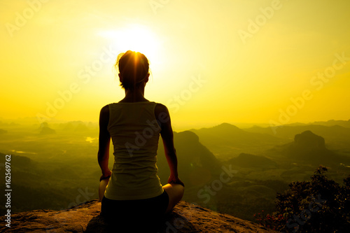 young fitness woman meditating on sunrise mountain peak