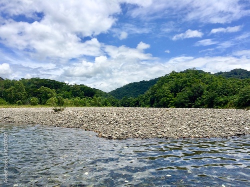 Bamboo rafting on the beautiful tropical Rio Grande river in the sunny Portland Parish of the island of Jamaica (Caribbean) with lush greenery and stone sand bed on a summer day with cloudy blue sky