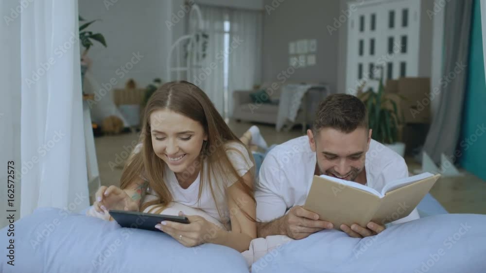 Young couple have leisure time lying in bed and reading book and tablet computer at home Young couple have leisure time lying in bed and reading book and tablet computer at home