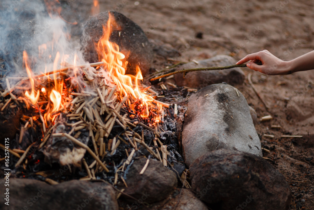 Female hand with a stick straightens the fire erupted on campings, outdoors Female hand with a stick straightens the fire erupted on campings, outdoors