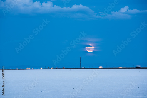 Bonneville White Salt Flats with highway and cars, while pink supermoon rises