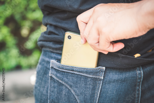 Thief is stealing smartphone from blue jeans pocket