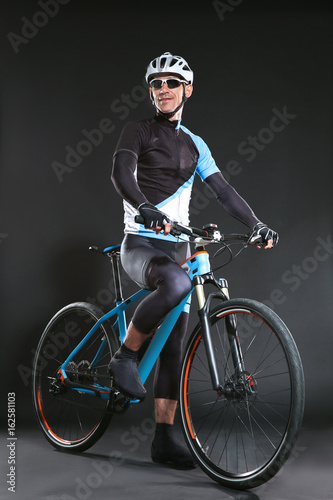 Fototapeta Naklejka Na Ścianę i Meble -  Young sporty cyclist with bicycle on dark background