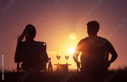 Couple relaxing outdoors having a glass on wine while watching the sunset. 