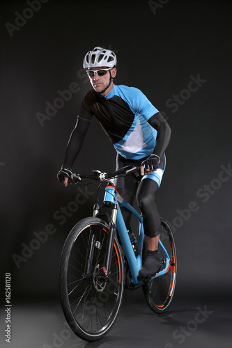 Fototapeta Naklejka Na Ścianę i Meble -  Young sporty cyclist riding bicycle on dark background