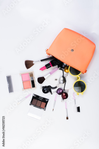 Top view of a make up bag, with cosmetic beauty products spilling out onto a white background.