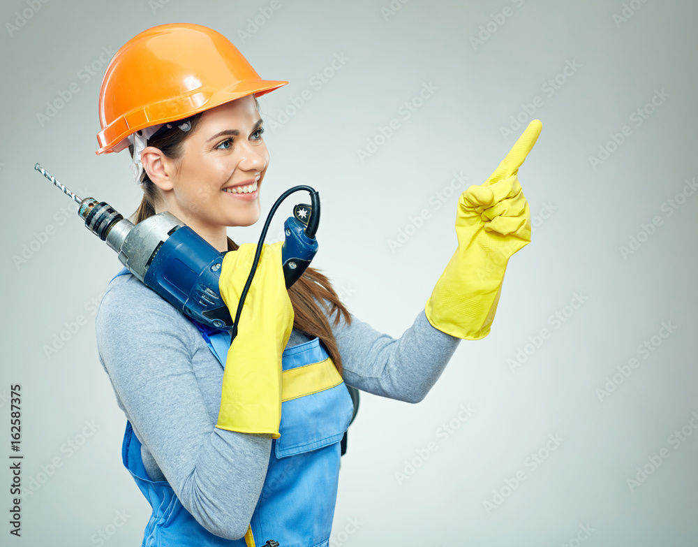 Smiling woman builder with building tool pointinf finger on copy space.