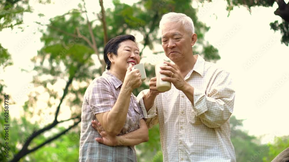 Asian senior couple showing affectionate and care through a cup of coffee in morning bright natural park Asian senior couple showing affectionate and care through a cup of coffee in morning bright natural park