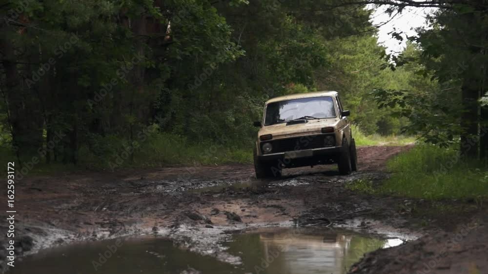 Dirty and mud-splattered car is riding through dirt, mud and puddles on a road in the forest. Dirty and mud-splattered car is riding through dirt, mud and puddles on a road in the forest.