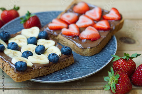 Two sweet sandwiches with blueberry, heart shaped banana and strawberry, chocolate spread and whole grain bread. Breakfast food