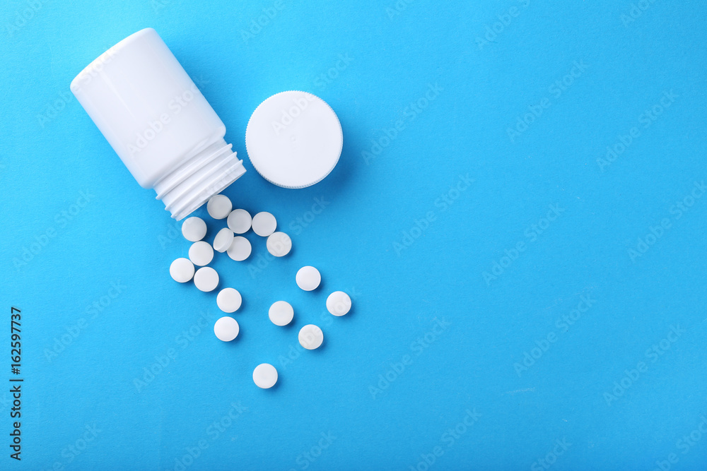White pills in plastic bottle on blue background