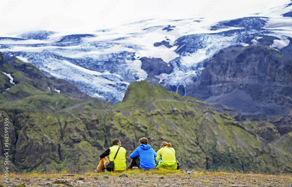 Fototapeta premium Group of hikers sitting on a ledge of a mountain, enjoying the beautiful view valley in Thorsmork, Iceland