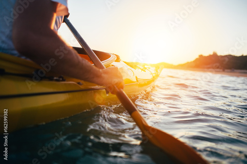 Fototapeta Close up of man holding kayak paddle at sunset