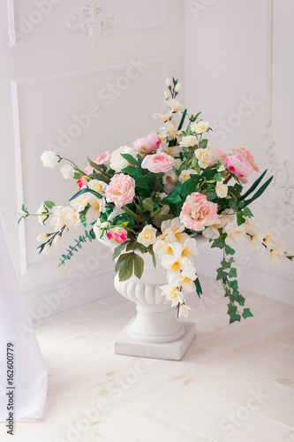 A bouquet of peonies and roses in a clay white jug on the floor at the threshold of the French window. Bright interior photo