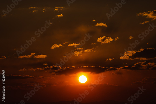 Dramatic sunset sky with orange colored clouds and sun.