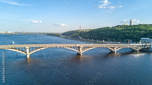 Aerial top view of Metro railway bridge with train and Dnieper river from above, skyline of city of Kiev, Ukraine 