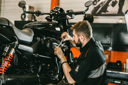 Professional mechanic working screwdriver and motorcycle repairs. Handsome young man repairing motorcycle in repair shop.