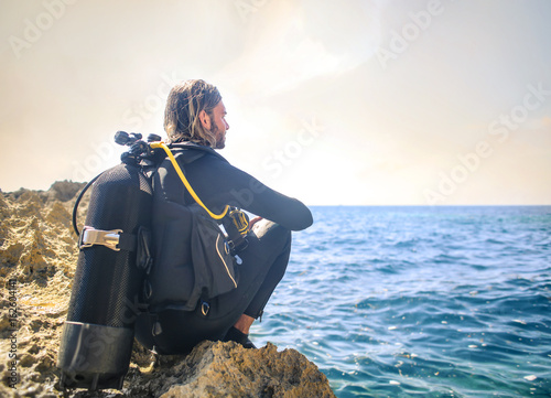 Scuba diver sitting on a rock, looking the sea