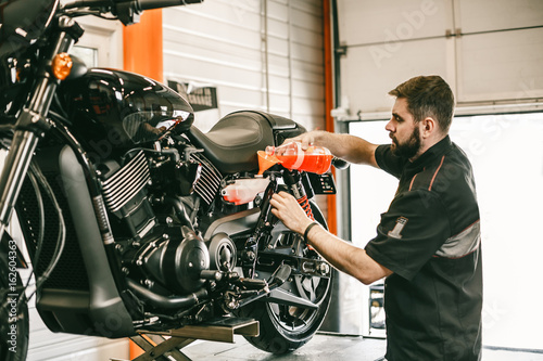 Professional mechanic pouring antifreeze into a motorcycle. Confident young man repairing motorcycle in repair shop.