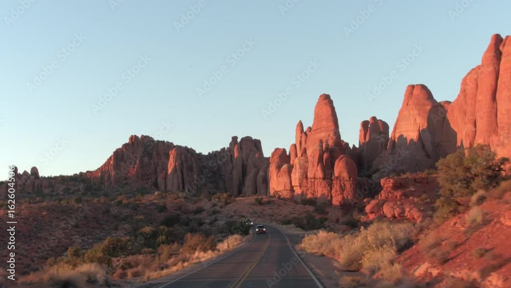 FIRST PERSON VIEW: Driving along an empty road through stunning Arches National Park in Utah on sunny morning. Curvy road winding past amazing red rock sandstone formations in hot desert at sunset.