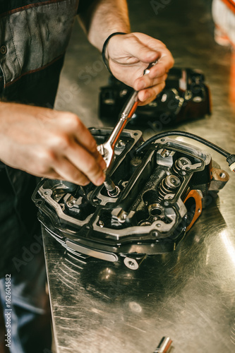 Closeup hands of motorcycle mechanic engine repair at service station. Handsome young man repairing motorcycle in repair shop.