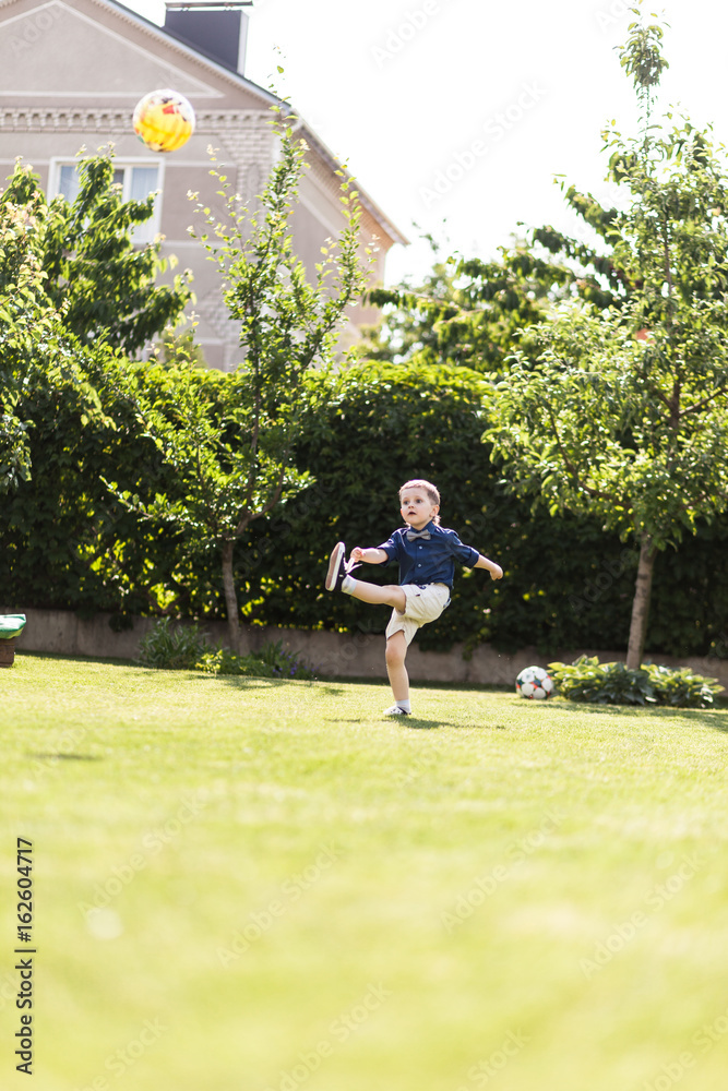 Stylishly dressed boy playing with a ball on a green lawn