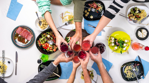 family clanging glasses by the table full of different tasty dishes, top view