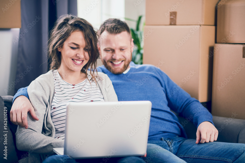 Couple using laptop in new apartment while sitting on sofa