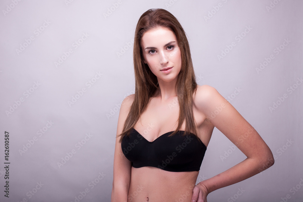Beautiful woman in bra with natural make up on gray background in studio photo. Beauty and fashion.