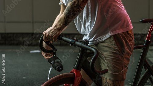 Tattooed biker hipster man in shorts winding the bar tape on a fixed gear bike handlebar