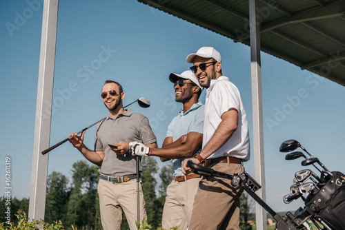 Three smiling men in sunglasses holding golf clubs outdoors