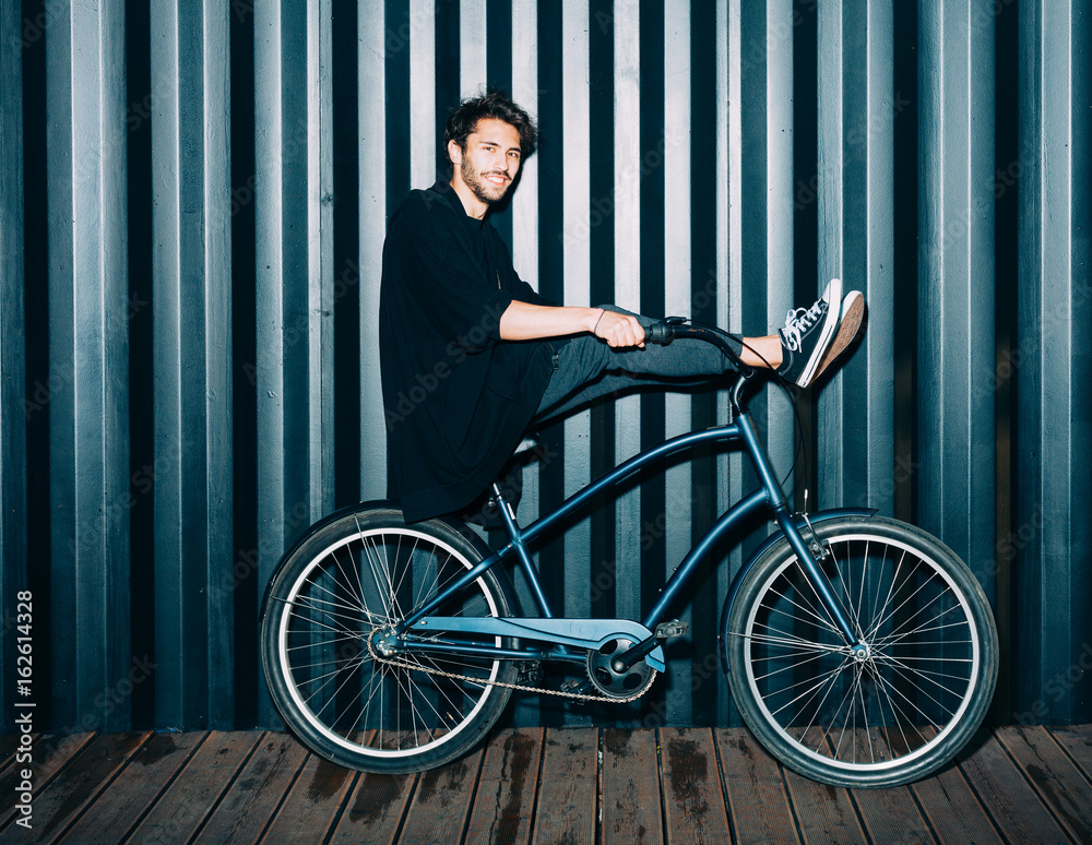 fun. Night portrait of a young man in a fashionable black outfit, laid his feet on the steering wheel of a vintage bicycle. fun. Night portrait of a young man in a fashionable black outfit, laid his feet on the steering wheel of a vintage bicycle.