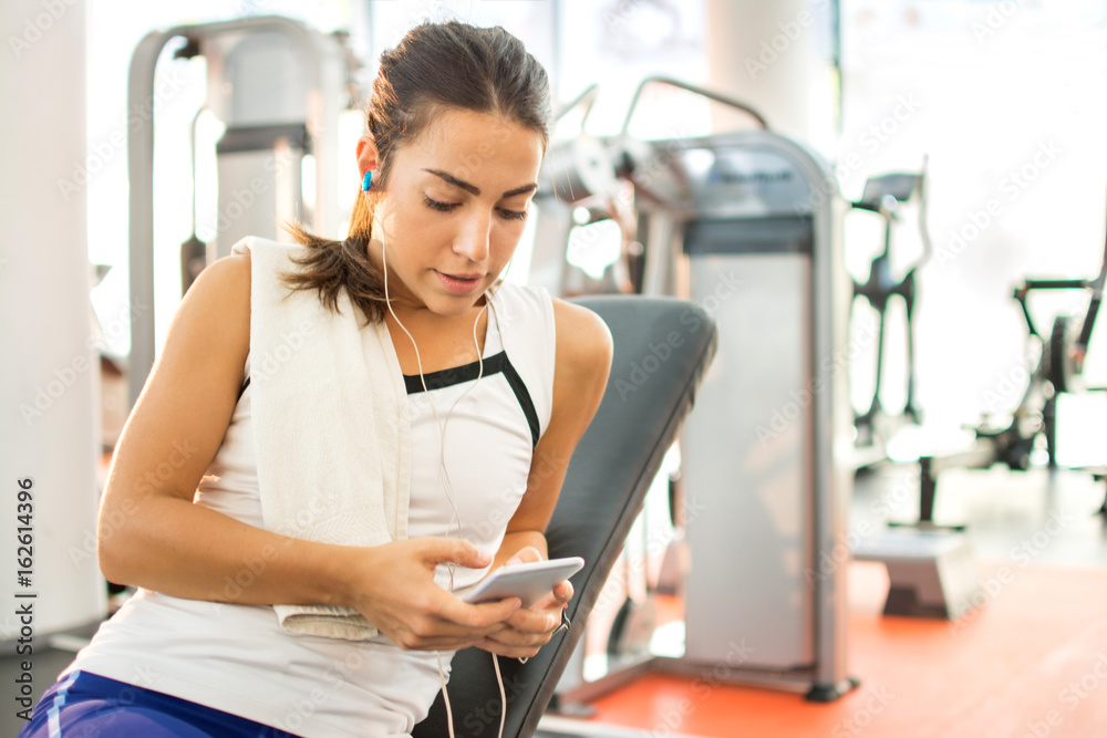 Young sporty woman with earphones and smartphone at the gym. Young sporty woman with earphones and smartphone at the gym.
