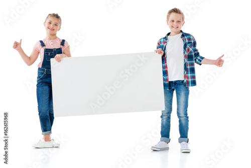 Adorable boy and girl holding blank banner and showing thumbs up sign