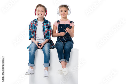 children listening music in headphones while sitting on cube together isolated on white © LIGHTFIELD STUDIOS