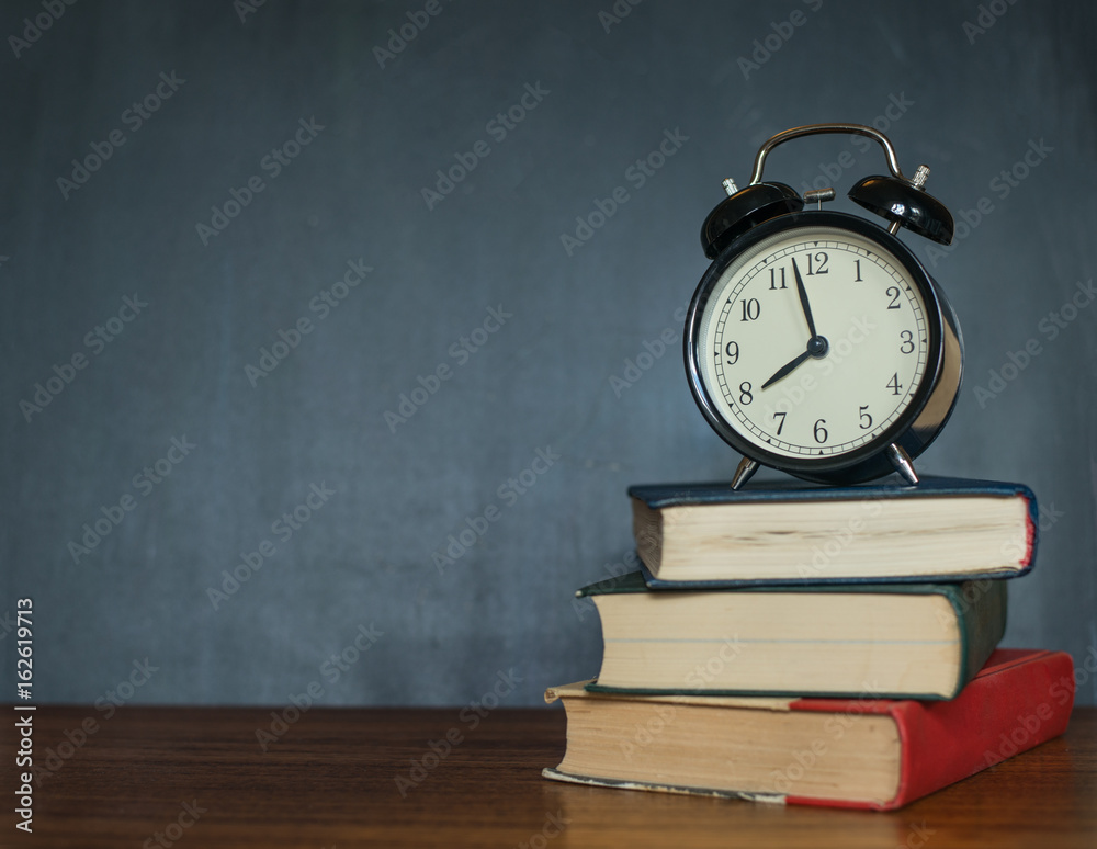Books and an alarm clock stand on the background of a school board Books and an alarm clock stand on the background of a school board