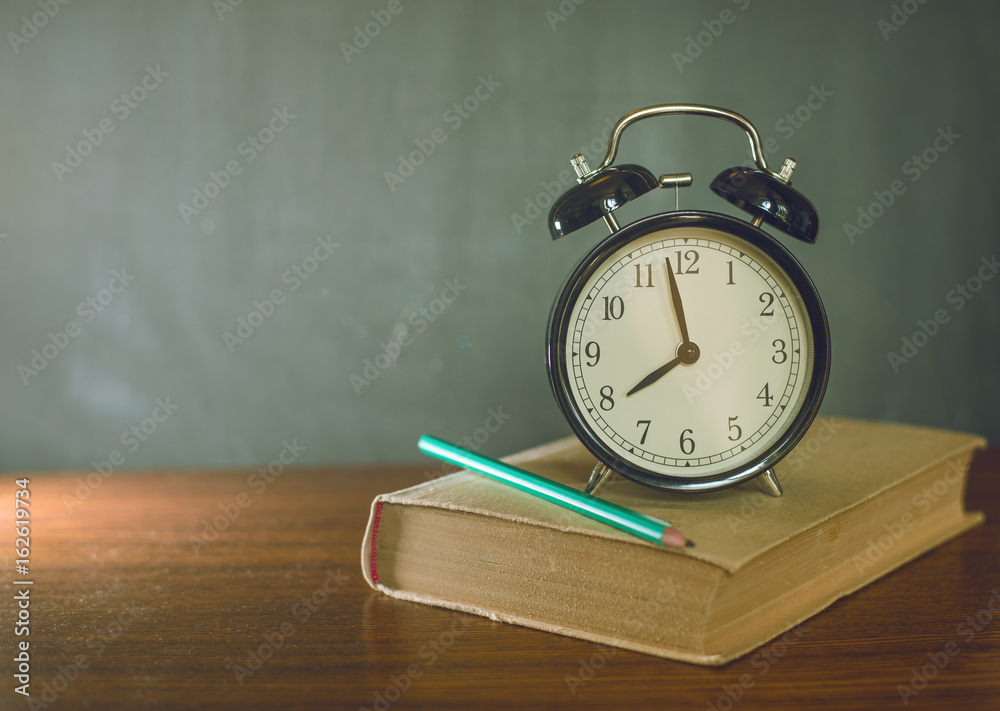 Books and an alarm clock stand on the background of a school board Books and an alarm clock stand on the background of a school board