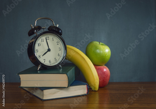 Books and alarm clock and fruits lie on the background of a school board