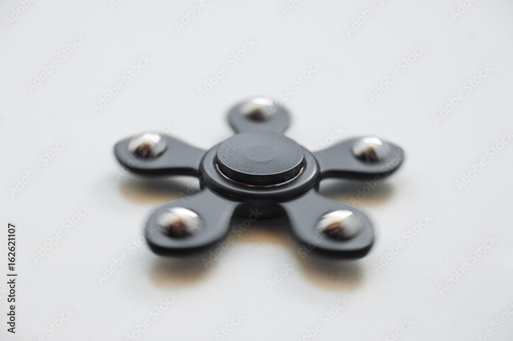 Black spinner on a white background. Black spinner with metal bearings spins on a white background. Aluminum alloy toy for fun and stress relief for office workers and ordinary employees Black spinner on a white background. Black spinner with metal bearings spins on a white background. Aluminum alloy toy for fun and stress relief for office workers and ordinary employees